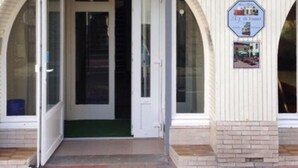 A building entrance with a white facade, a brick-paved entrance, and a signboard with a logo and text. - Auberge Riva Bella - Hostel (Le Touquet-Paris-Plage)