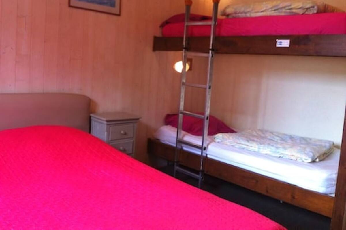 Een slaapkamer met een stapelbed, een nachtkastje en een rode dekbedovertrek.