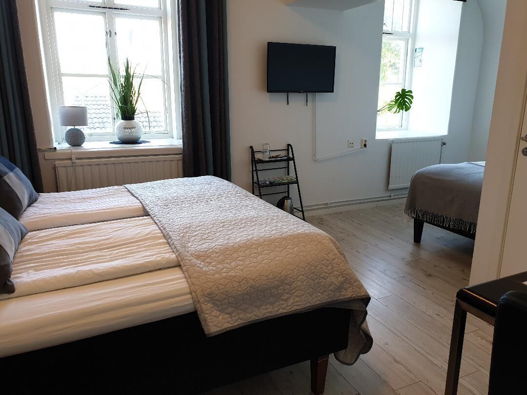 Ein Schlafzimmer mit einem Bett, einem an der Wand montierten Fernseher, einem Fenster mit Vorhängen und einer Heizung.