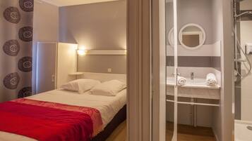 Une chambre à coucher avec un lit, une couverture rouge et une salle de bain avec un lavabo et un miroir.