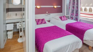 Ein Hotelzimmer mit zwei Betten, einem Badezimmer und Blick auf ein Gebäude.