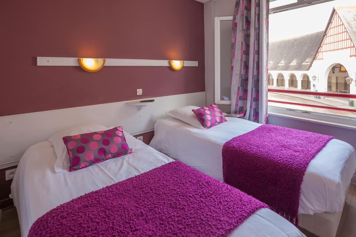 Une chambre d’hôtel avec deux lits, chacun doté d’un matelas blanc et d’une couverture violette. Deux appliques murales sont fixées au-dessus des lits.