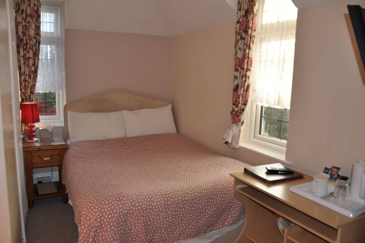 A bedroom with a bed, a desk, a lamp, and a window with curtains.