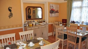 Un comedor con una mesa de madera dispuesta para cuatro, un espejo sobre la mesa y vista a la calle a través de una ventana.