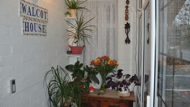 Un rincón de una habitación con un cartel que dice 'WALCOT HOUSE', una planta en maceta y una ventana con cortina.