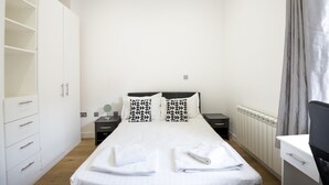 Une chambre bien rangée, avec un grand lit, deux tables de chevet, une armoire et un bureau.