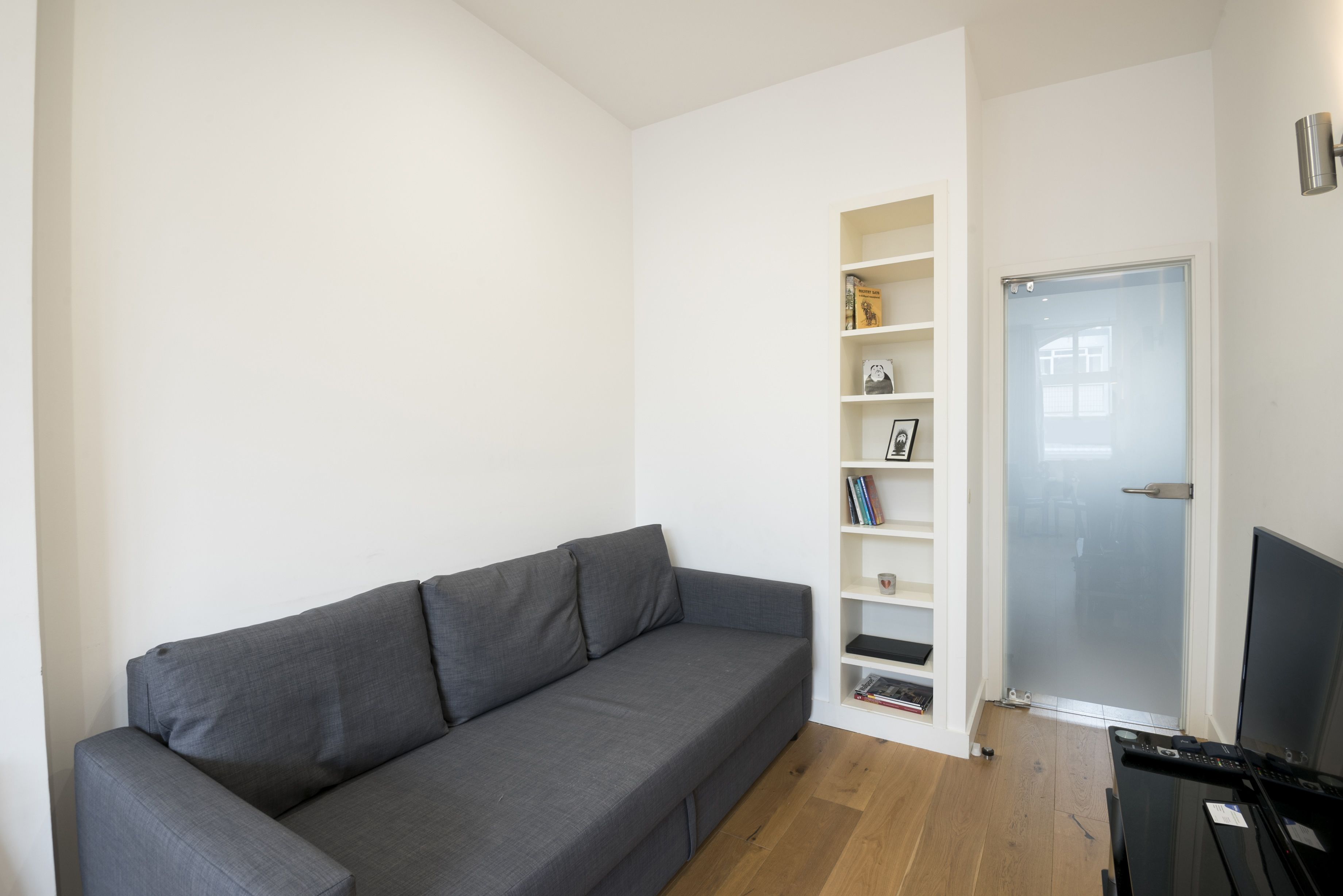 A modern living room with a grey sofa, a bookshelf, and a door leading to another room.