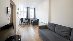 Un salon moderne avec un canapé gris, un coin repas comprenant une table et des chaises, et un téléviseur fixé au mur.