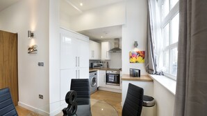 Une cuisine moderne avec des meubles blancs, un four à micro-ondes, un four et un lave-linge. On y trouve une table à manger avec des chaises et une fenêtre avec des rideaux.