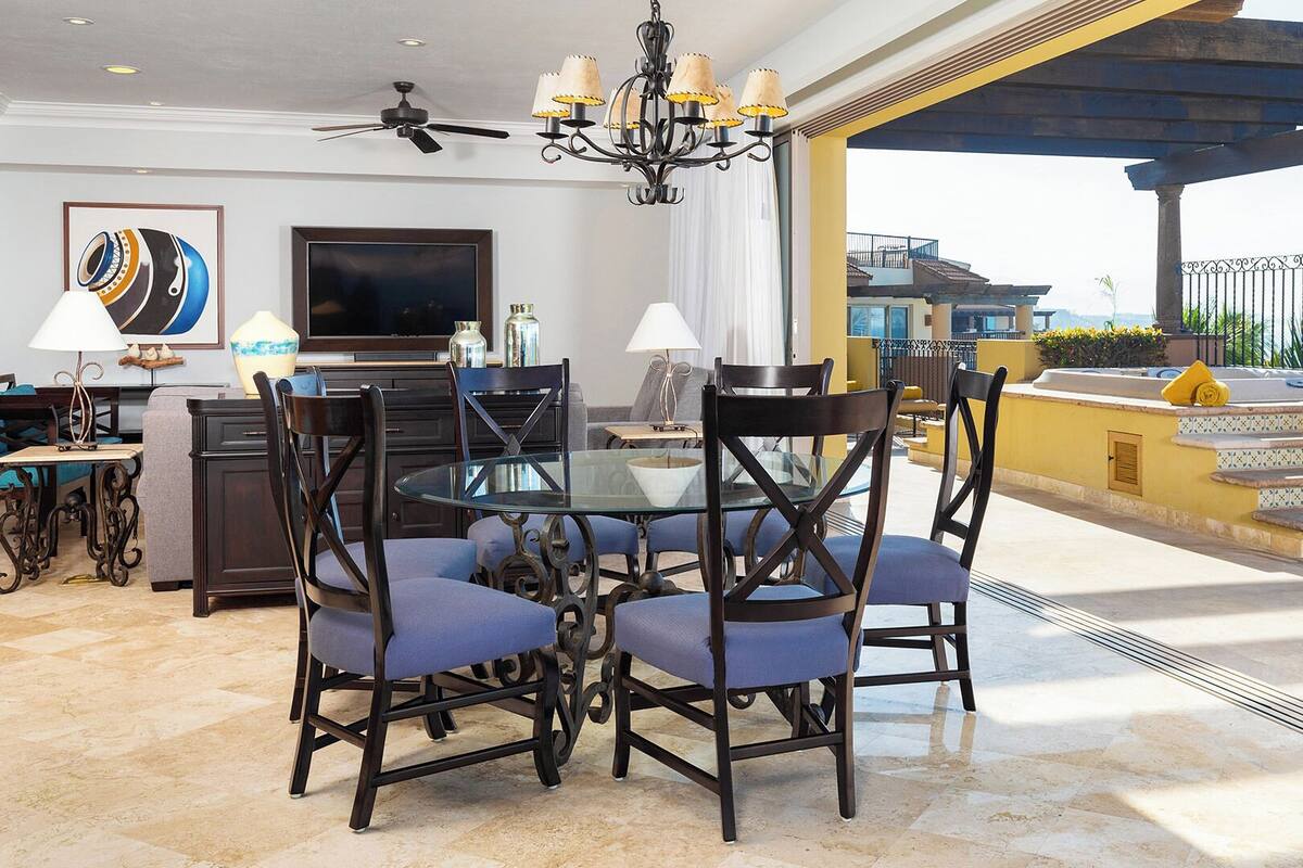 Een eethoek met een ronde glazen tafel, donkerhouten stoelen en een plafondventilator.