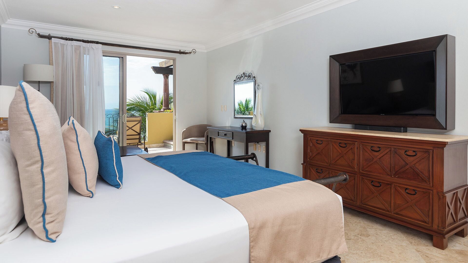 A hotel room with a bed, a TV, a desk, and a view of the outdoors.