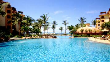A large swimming pool surrounded by palm trees and resort buildings.