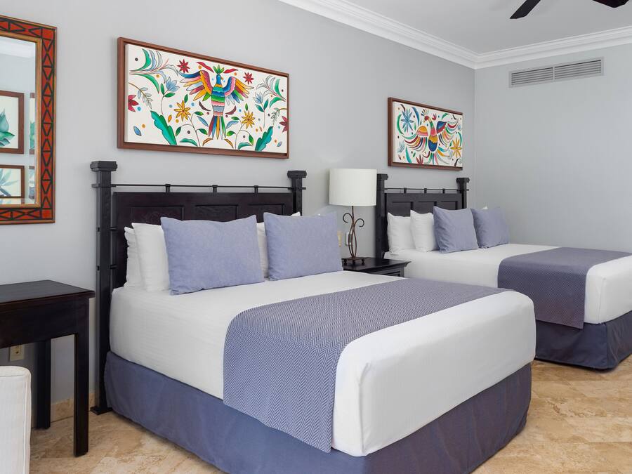A hotel room with two beds, a desk, and artwork on the walls.