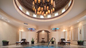 Una amplia piscina interior con una fuente central, rodeada de sillones de descanso y plantas en macetas.