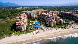 Un resort con varias edificaciones, un área de piscina central y una playa.