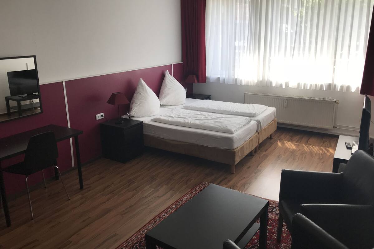 A hotel room with a bed, a desk, a chair, a TV, and a window with curtains.