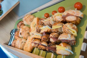 Una bandeja con una variedad de pasteles y sándwiches, incluyendo croissants, bagels y sándwiches con diferentes ingredientes.
