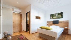 A modern bedroom with a wooden floor, a bed with white bedding and a green pillow, a mounted TV, and a framed picture on the wall. - Aparthotel Nah dran (Loiching)
