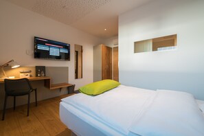 Una habitación de hotel moderna con cama, escritorio, silla, televisor y armario.
