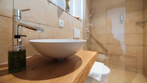 A bathroom with a wooden vanity, a white basin, and a bottle of liquid soap. - Aparthotel Nah dran (Loiching)