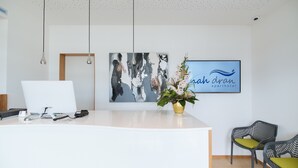 A reception desk with a computer, a framed abstract painting, and a logo for 'rah dran apartment hotel'. - Aparthotel Nah dran (Loiching)