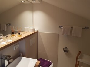 A modern bathroom with a wooden vanity, a white sink, a mirror, and a shower area. - Gästehaus Gerold (Bad Kohlgrub)