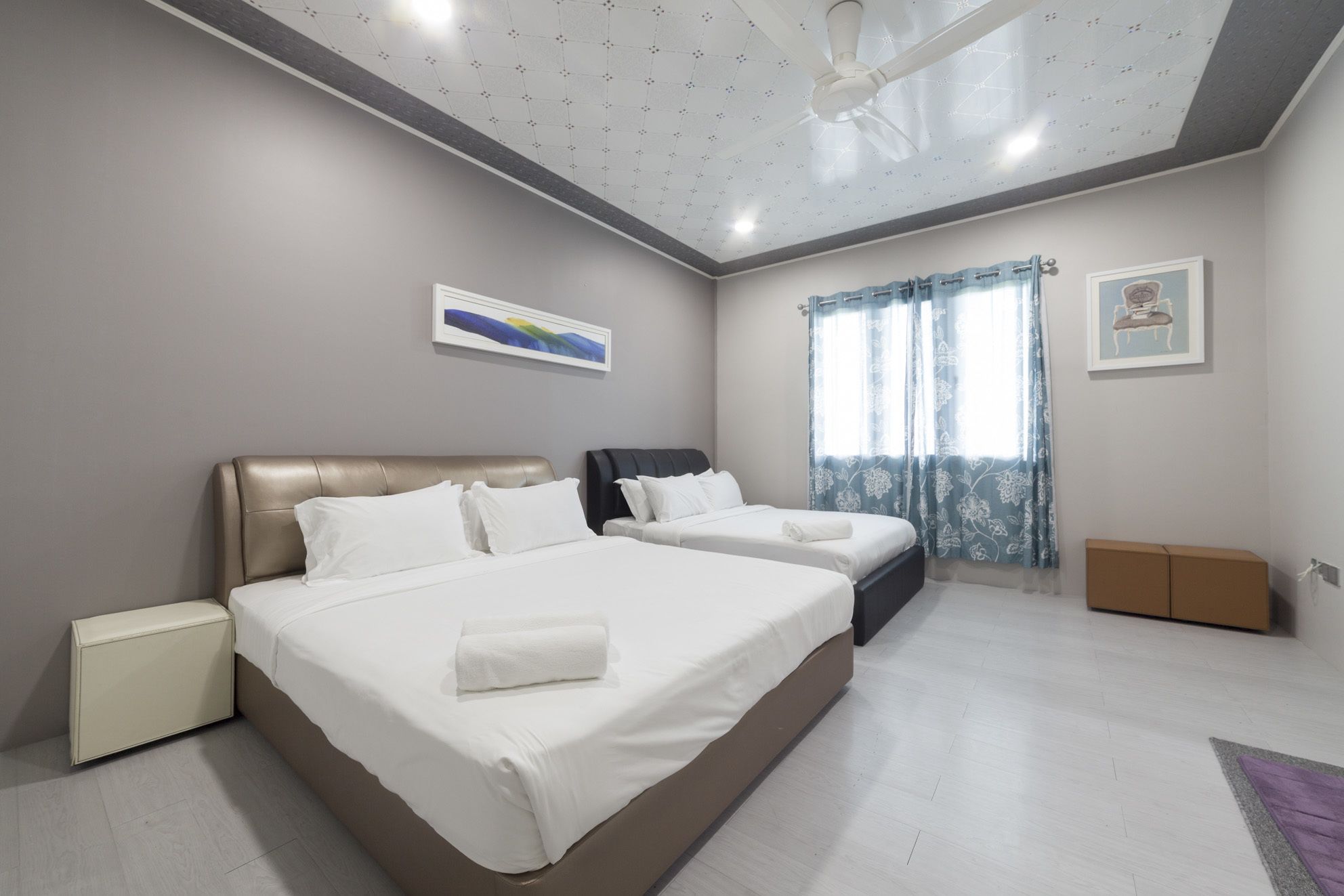 Habitación de hotel con dos camas, ventilador de techo, ventana con cortinas y un armario pequeño.