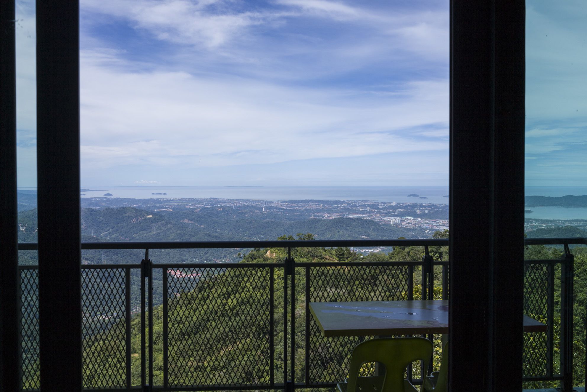 A balcony with a table and chair, overlooking a coastal cityscape with a clear sky.