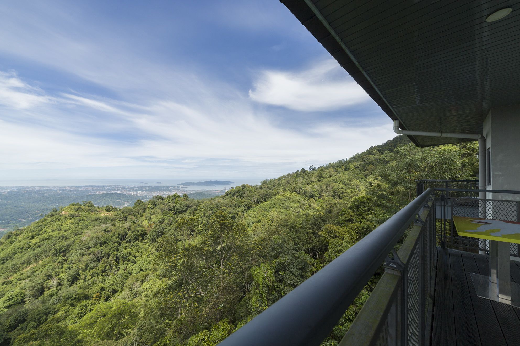 Un balcón con vistas a una ladera verde y exuberante y un paisaje urbano distante.