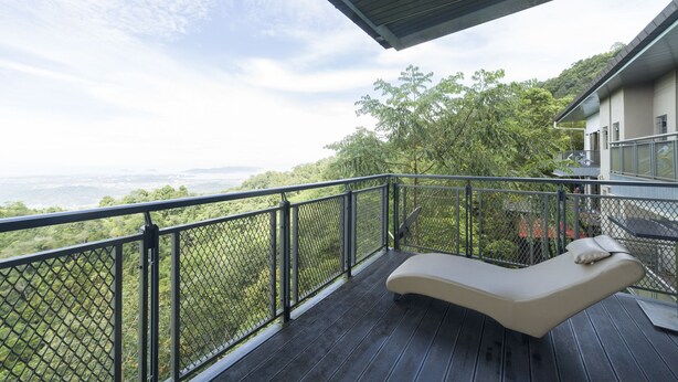 Un balcone con una poltrona imbottita, ringhiera in metallo e vista su un paesaggio verde.