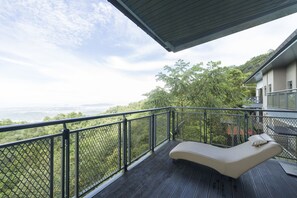 A balcony with a cushioned lounge chair, a metal railing, and a view of a green landscape. - Kokol Heights Villa (Kota Kinabalu)