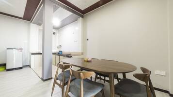 A dining area with a wooden table and four chairs, a refrigerator, and a kitchen area in the background.
