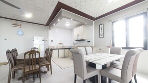 Un'area pranzo con tavolo e sedie in legno, una cucina sullo sfondo e un'ampia finestra che lascia entrare luce naturale.