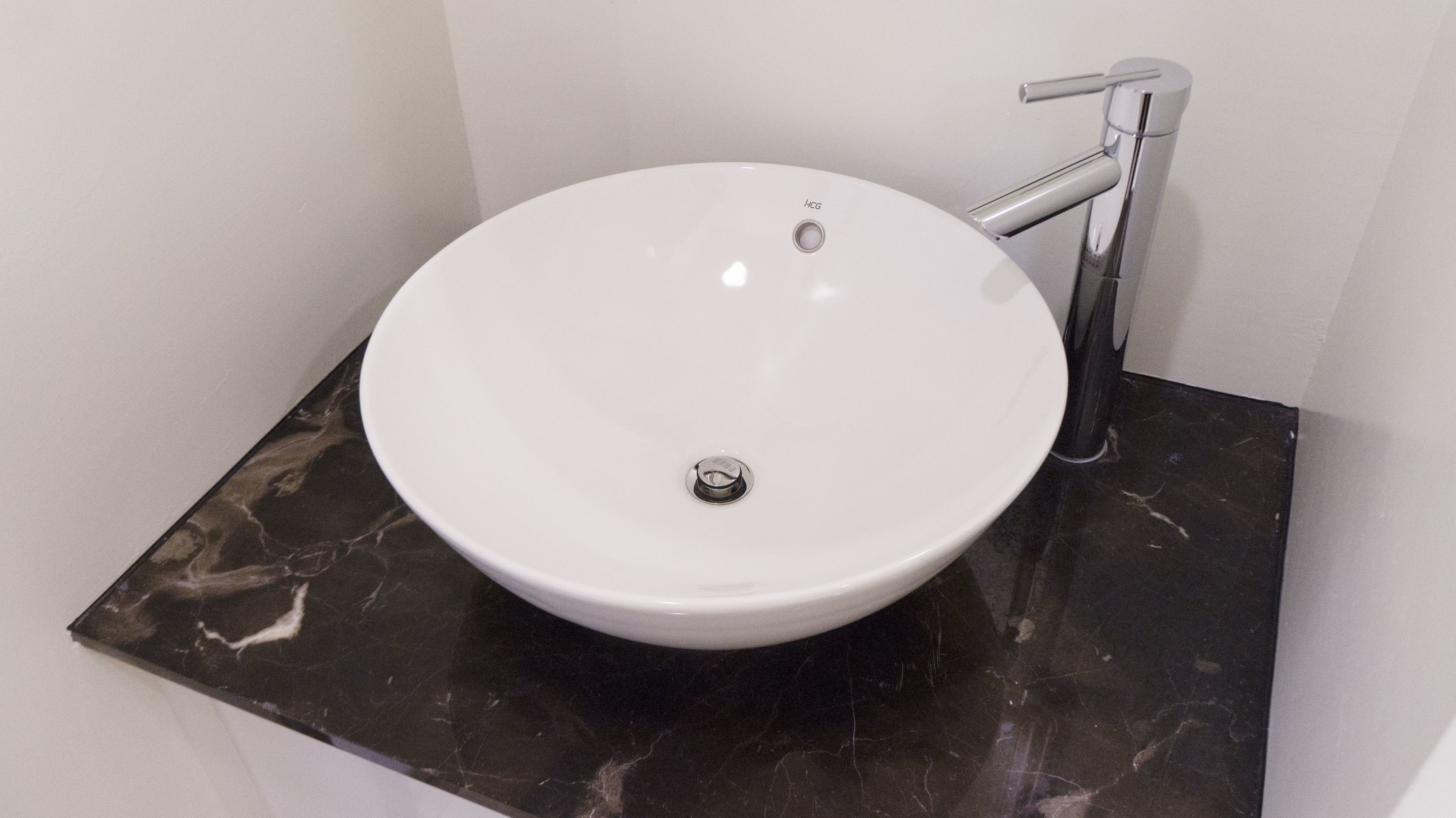 Ein weißes Waschbecken mit einem einzelnen Wasserhahn auf einer schwarzen Marmorarbeitsplatte in einem Badezimmer.