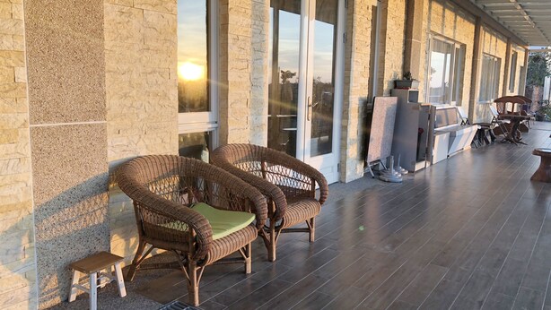 Un espace extérieur abrité, aménagé avec des fauteuils en osier, un petit tabouret et une table avec des chaises.