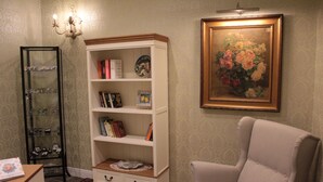 Una habitación con una estantería blanca, un sillón color beige y un cuadro con flores en la pared.