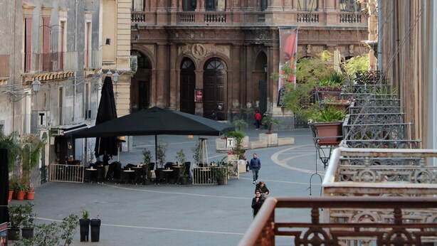 Un edificio histórico con arquitectura ornamentada, un patio con mesas al aire libre y vista a la calle.