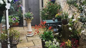A courtyard with a stone wall, a wooden shed, and various potted plants and flowers. - Victoria House Room Only Accommodation (Caernarfon)