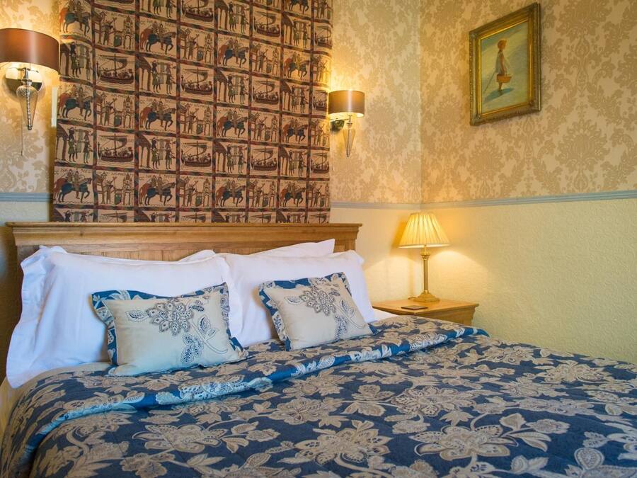 A neatly made bed with a floral-patterned bedspread and matching pillows, a headboard with a decorative panel, and two wall-mounted lamps.
