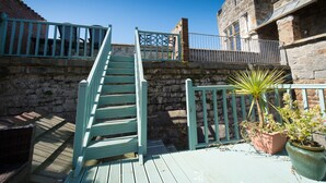 A wooden staircase leading to a balcony with a metal railing, a potted plant, and a stone wall. - Victoria House Room Only Accommodation (Caernarfon)