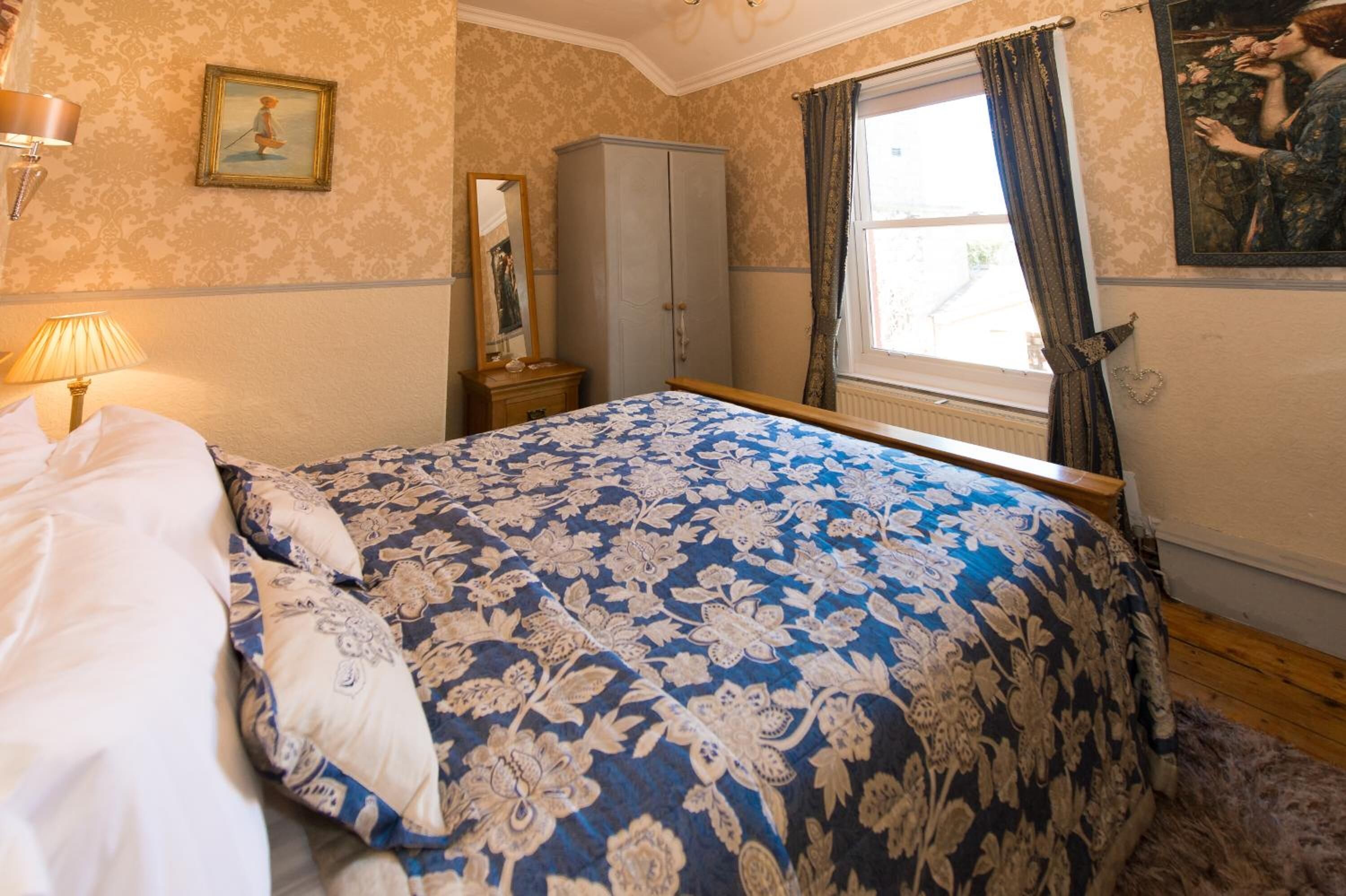 A bedroom with a large bed, a wardrobe, a mirror, and a window with curtains.
