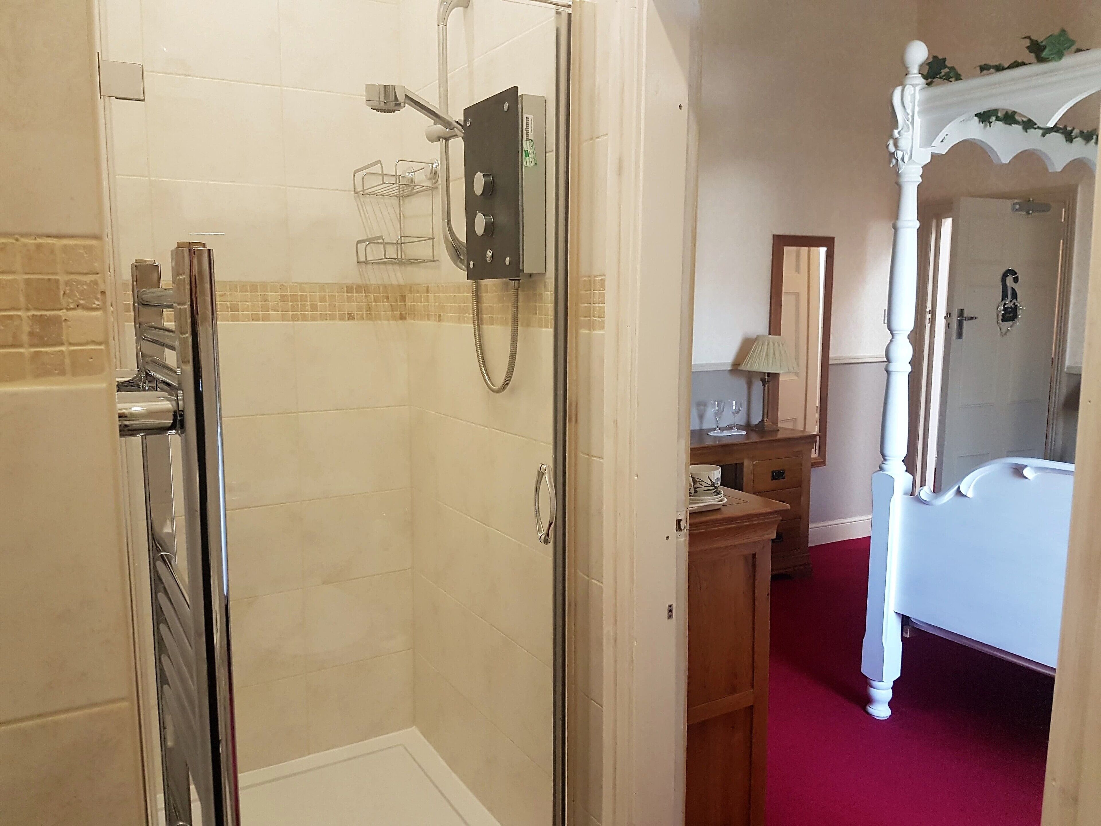 A bathroom with a glass-enclosed shower, a wooden vanity with a mirror, and a four-poster bed.