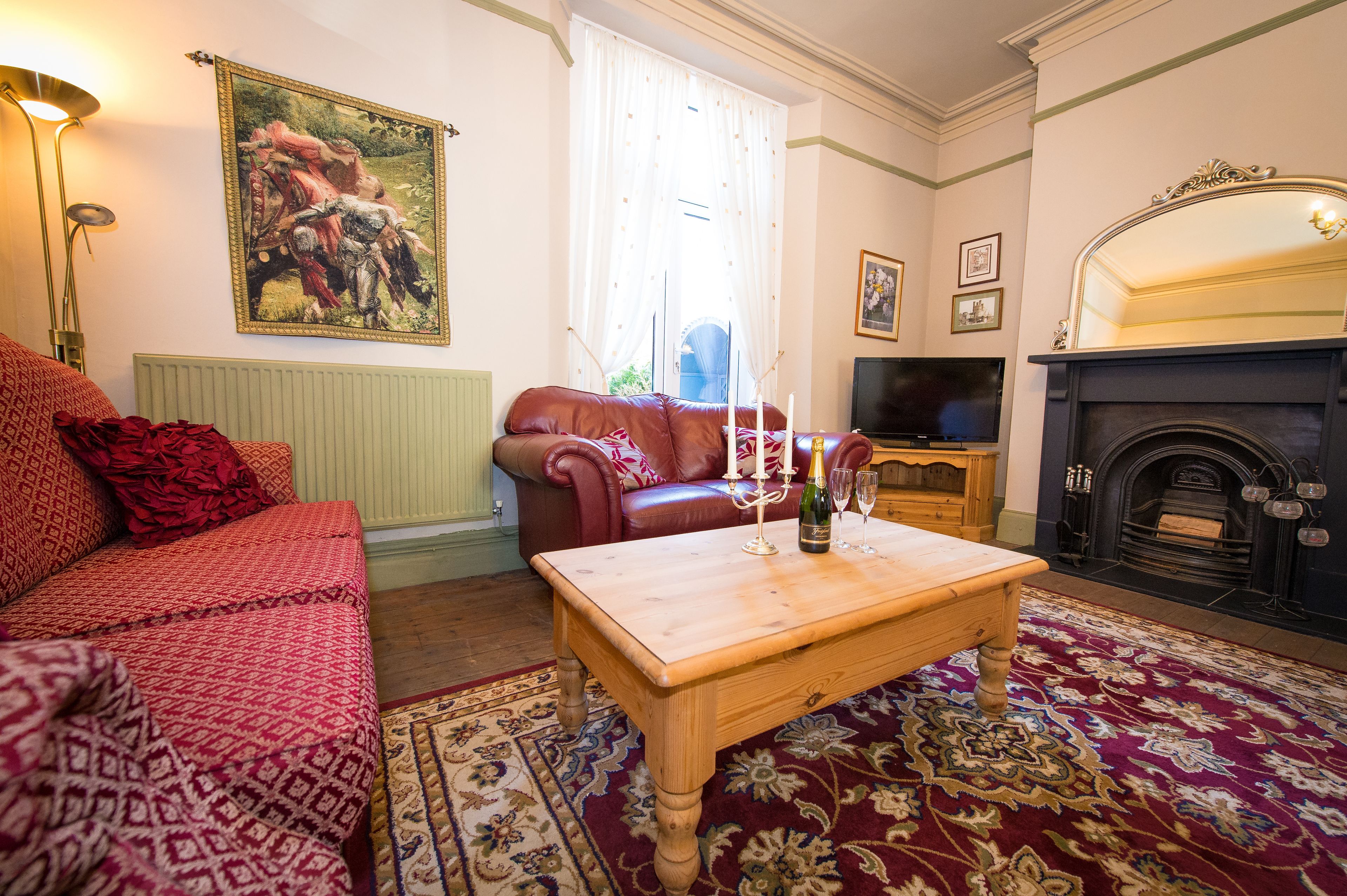 A living room with a red sofa, a wooden coffee table, a fireplace, and a painting on the wall.