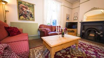 A living room with a red sofa, a wooden coffee table, a fireplace, and a painting on the wall.