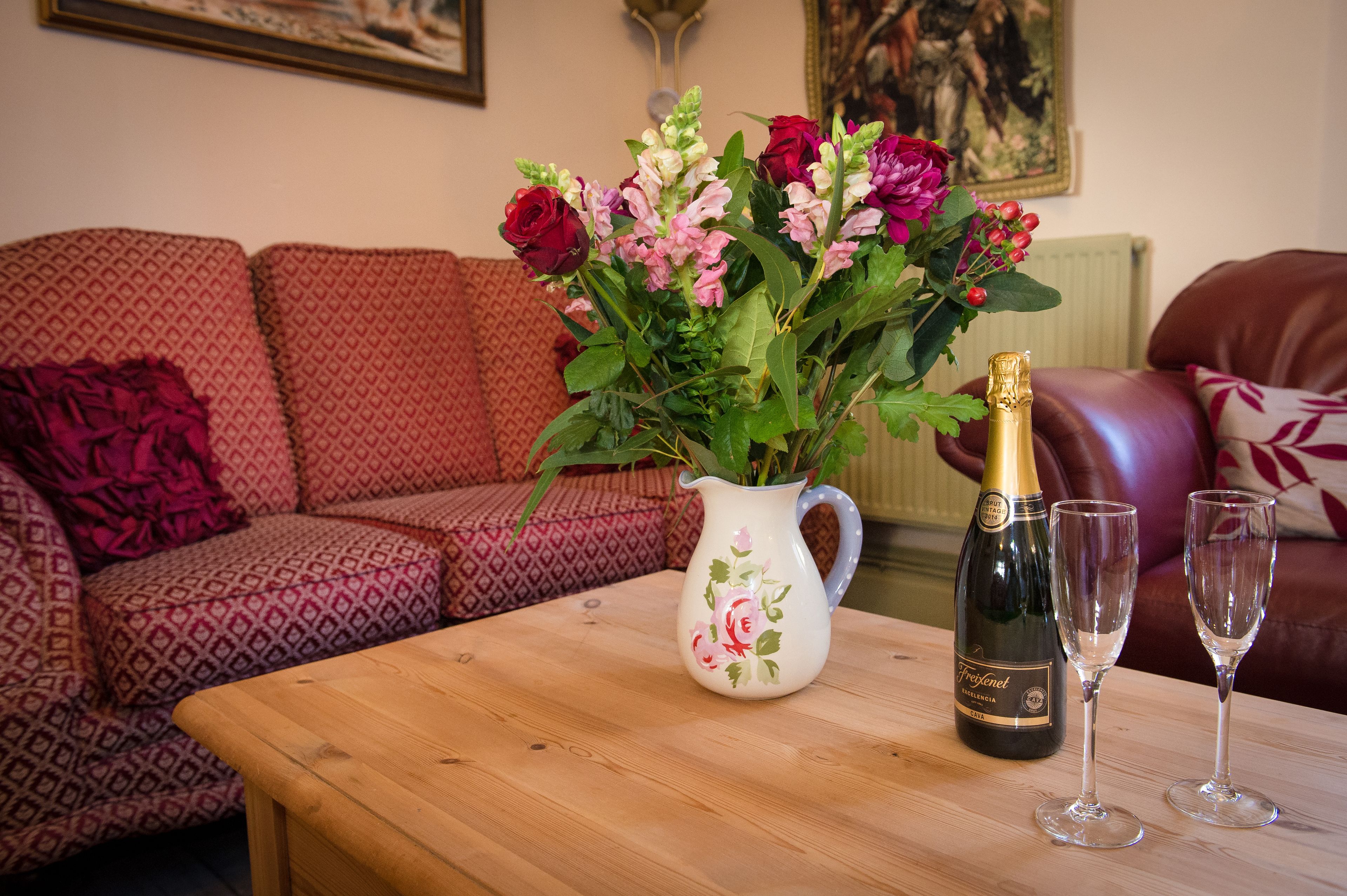 A living room with a wooden coffee table, a floral vase with flowers, a bottle of champagne, and two glasses.