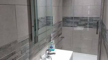 Ein modernes Badezimmer mit Duschkabine aus Glas, einem weißen Waschbecken und einem Spiegel darüber.