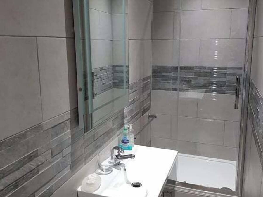 Ein modernes Badezimmer mit Duschkabine aus Glas, einem weißen Waschbecken und einem Spiegel darüber.