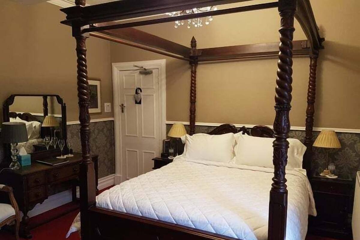A four-poster bed with a quilted white duvet, wooden headboard, and nightstands with lamps.