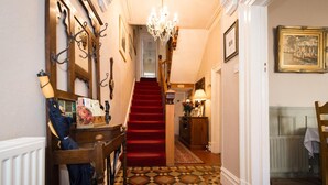 A hallway with a red carpet, a wooden chair, a chandelier, and a staircase leading to another room. - Victoria House Room Only Accommodation (Caernarfon)
