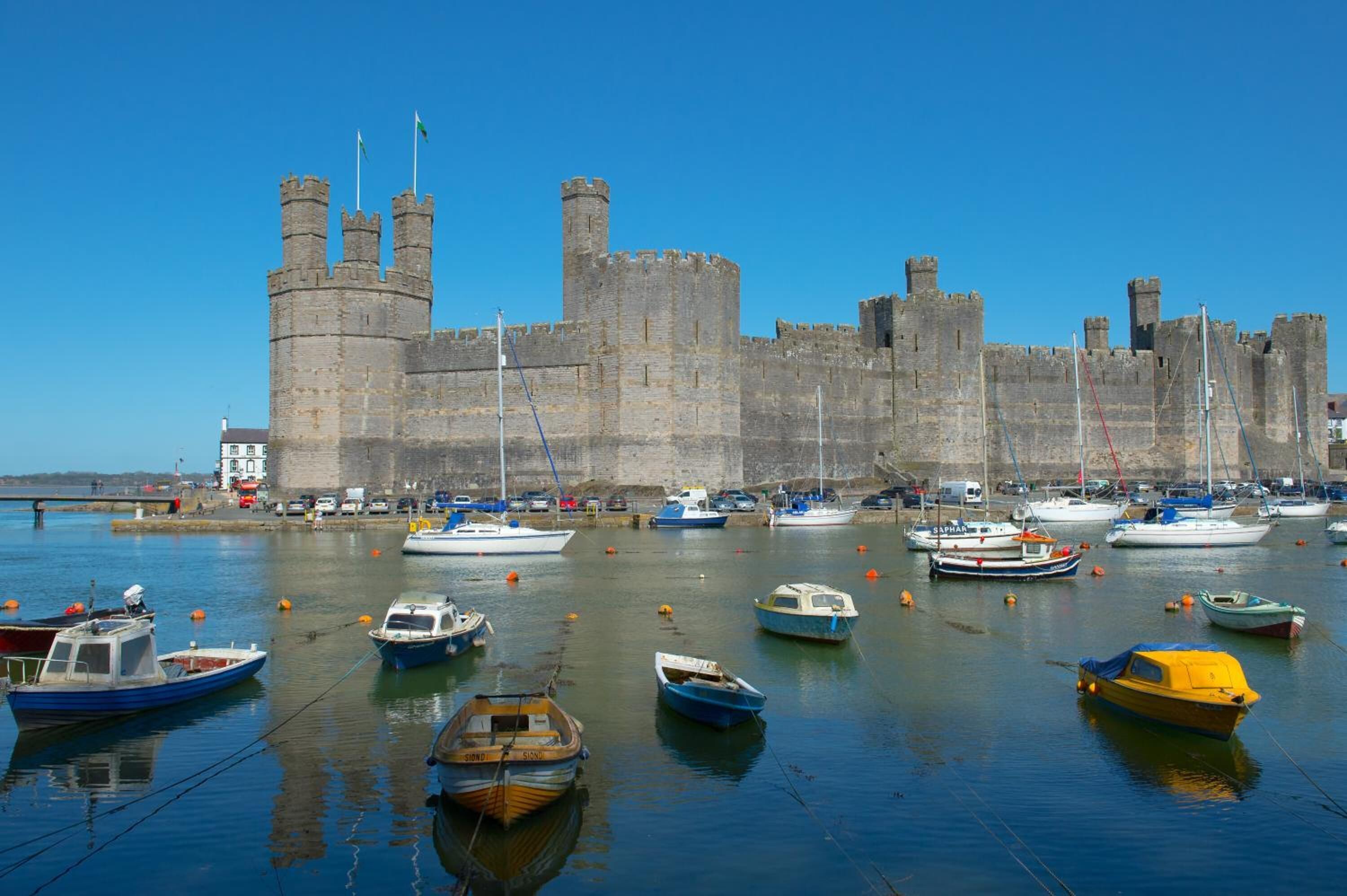 A historic castle with a moat and several boats docked in the water.